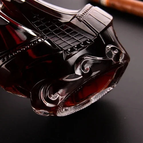 Carafe à whisky en forme de bateau inclinée sur une table avec un verre de whisky et un cigare en arrière-plan.