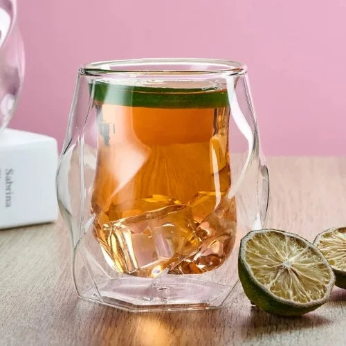 Verre à whisky au design original, rempli de whisky avec glaçons, tenu à la main sous un ciel bleu clair